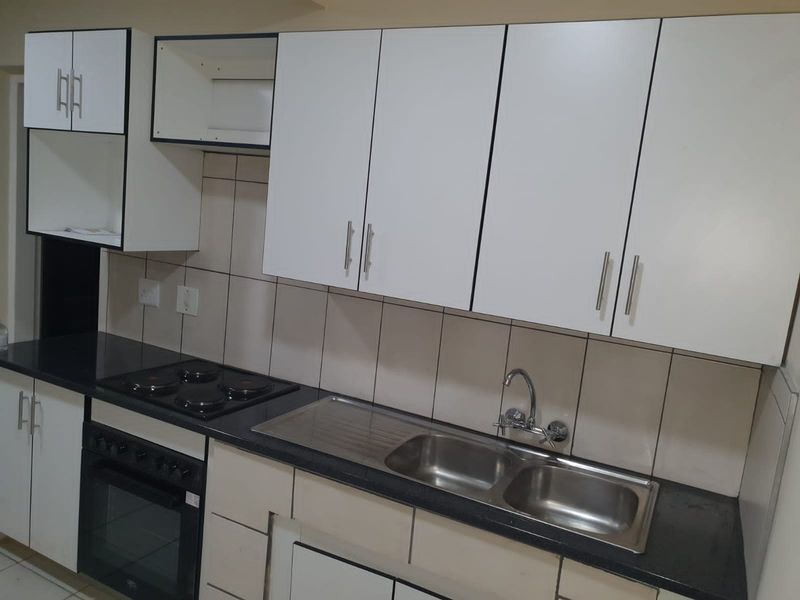 A functional kitchen featuring white cabinetry, dark countertops, a built-in oven, electric hob, and a stainless steel double sink with tiled backsplash.