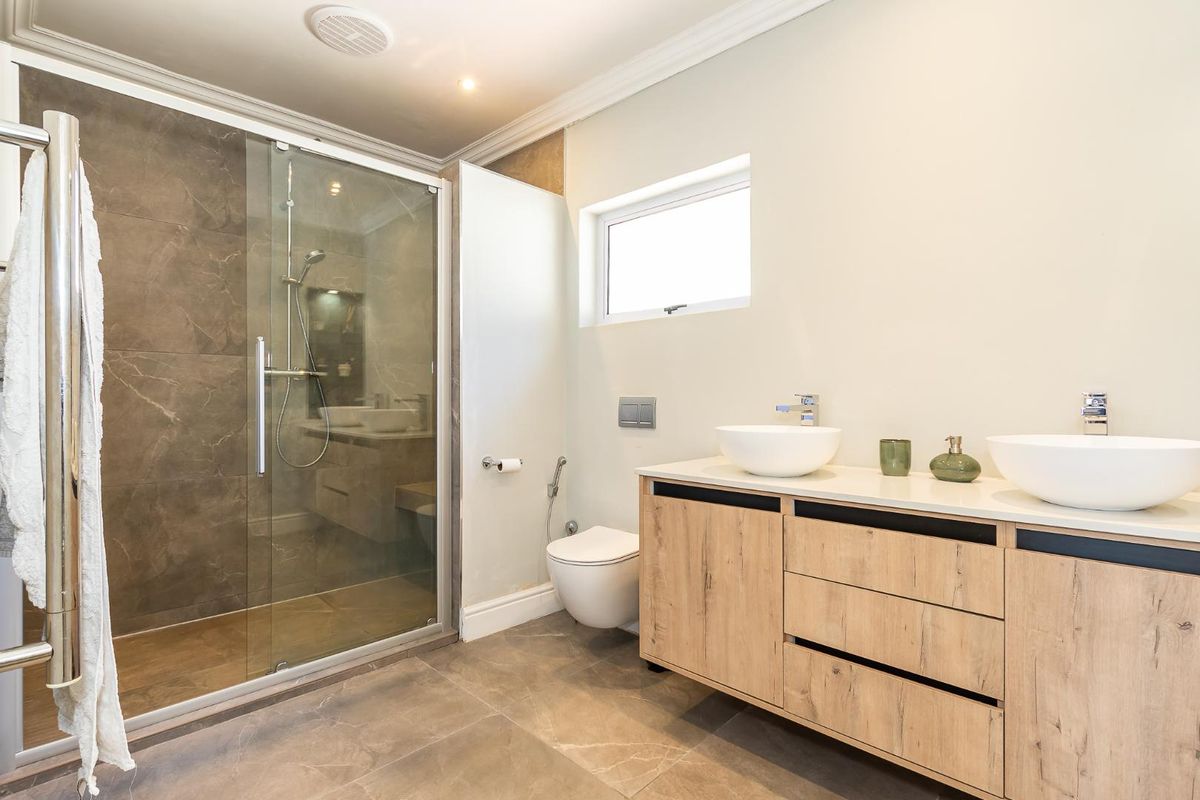 Modern bathroom featuring a glass-enclosed walk-in shower, wall-mounted toilet, and a double vanity with vessel sinks and wood-finish cabinetry.