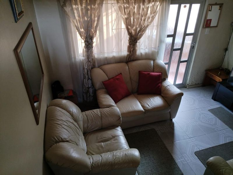 A living room area featuring tiled flooring, security gate access, and window security bars, showing signs of wear on the wall finishes.