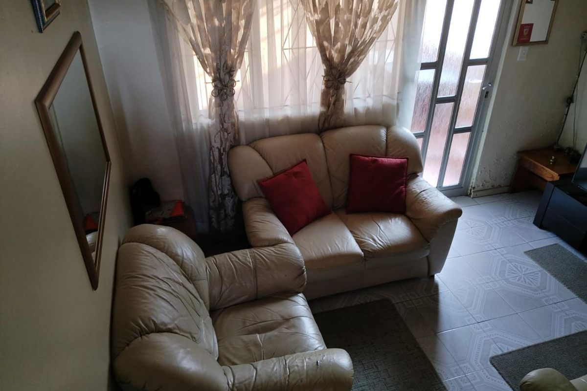 A living room area featuring tiled flooring, security gate access, and window security bars, showing signs of wear on the wall finishes.