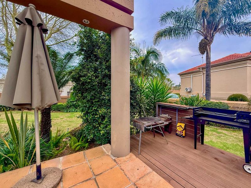 A covered outdoor patio area featuring a combination of terracotta tiling and wooden decking, overlooking a private garden space.