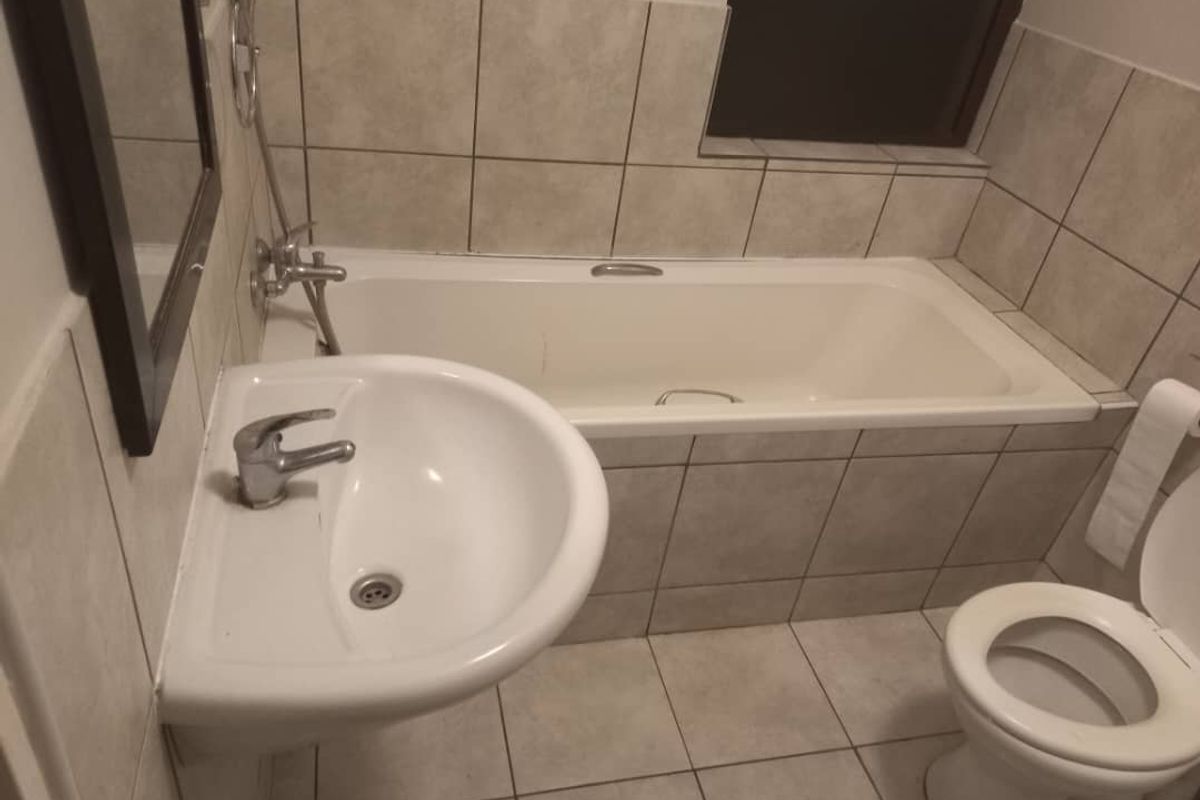 A functional bathroom featuring a built-in bathtub, pedestal basin, and toilet with neutral wall and floor tiling.