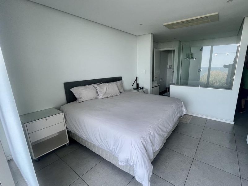 Modern bedroom featuring large format floor tiles, recessed ceiling lighting, integrated air conditioning unit, and an en-suite bathroom with glass partition walls.