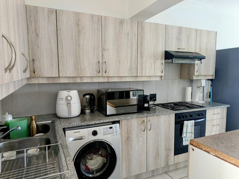 A functional kitchen featuring light wood-grain laminate cabinetry, granite countertops, a built-in oven with hob, and integrated laundry plumbing.