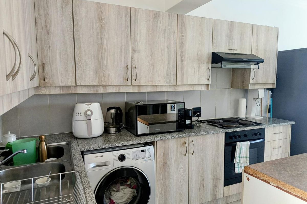 A functional kitchen featuring light wood-grain laminate cabinetry, granite countertops, a built-in oven with hob, and integrated laundry plumbing.