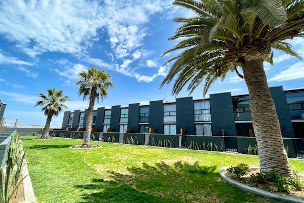 A well-maintained exterior view of the apartment complex featuring a landscaped lawn, mature palm trees, and modern dark-toned building facade.