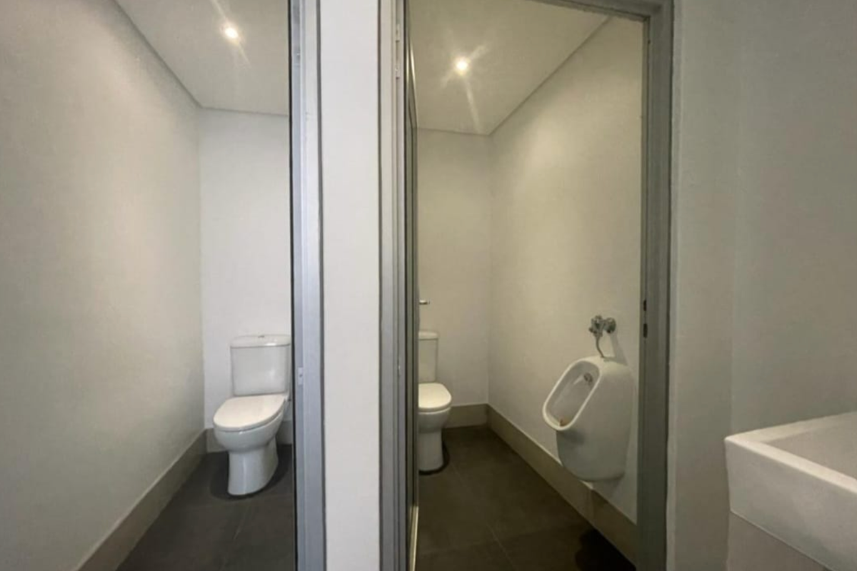 A functional office restroom facility featuring two separate toilet cubicles and a wall-mounted urinal with tiled flooring.