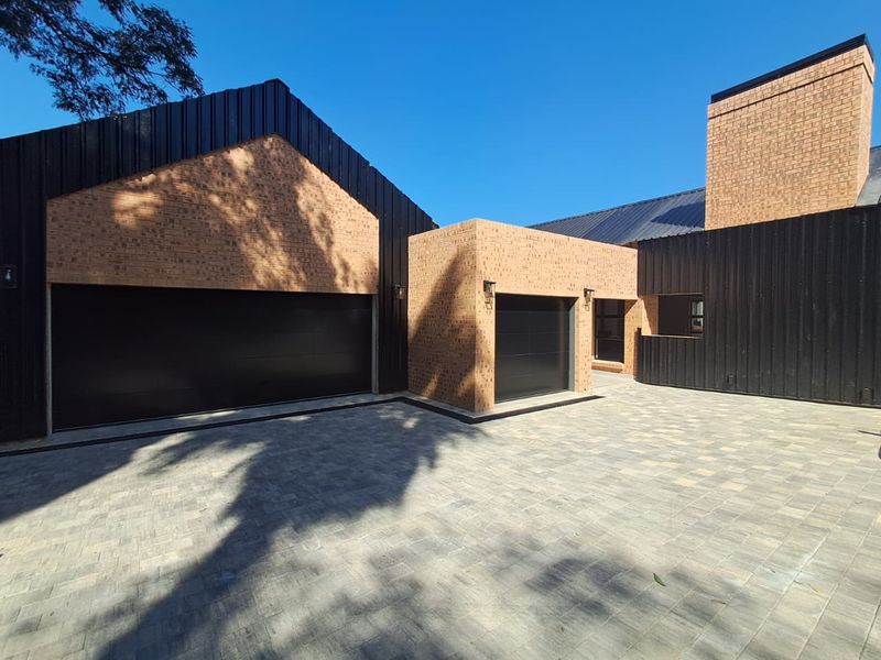 Modern architectural exterior featuring a combination of brick and dark metal cladding with a spacious paved driveway and multiple garage access points.