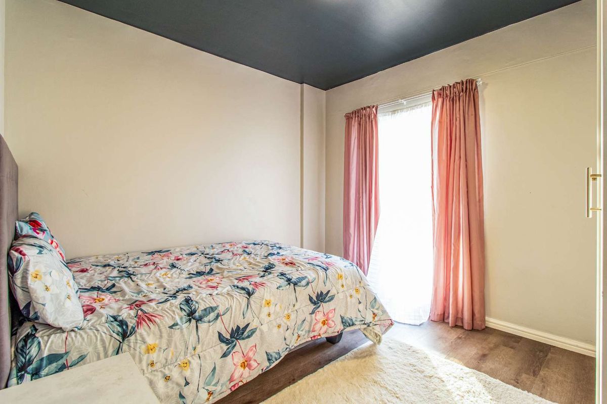 A bedroom featuring wood-look flooring, a dark-painted ceiling, and a window with curtain fixtures, providing a functional living space.