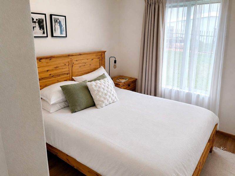 A well-maintained bedroom featuring laminate flooring and large windows with neutral curtains, providing a bright and comfortable living space.