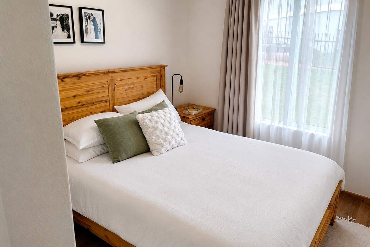 A well-maintained bedroom featuring laminate flooring and large windows with neutral curtains, providing a bright and comfortable living space.