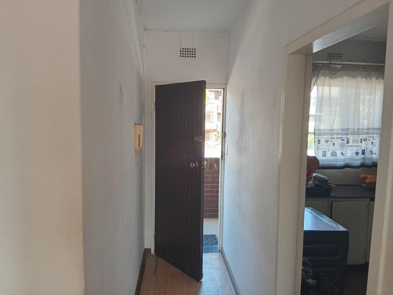 A narrow apartment hallway featuring laminate flooring, an intercom system, and access to the kitchen and exterior entrance.