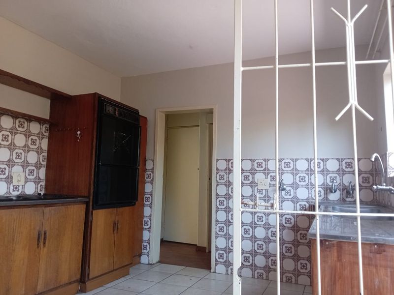 A dated kitchen featuring wooden cabinetry, a built-in oven, tiled backsplash, and a stainless steel sink, requiring modernization to improve aesthetic appeal.