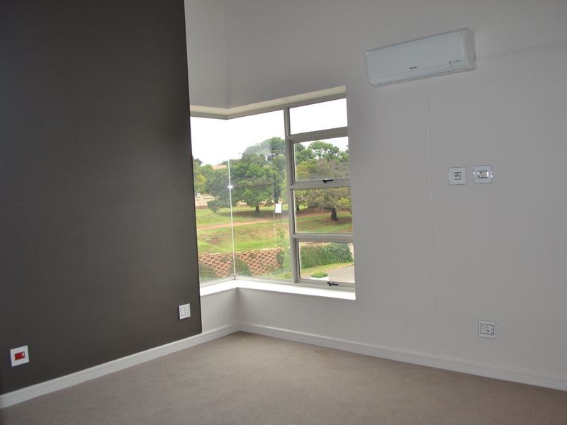 A bright, empty bedroom featuring a corner window, neutral carpeting, and a wall-mounted split-system air conditioner.
