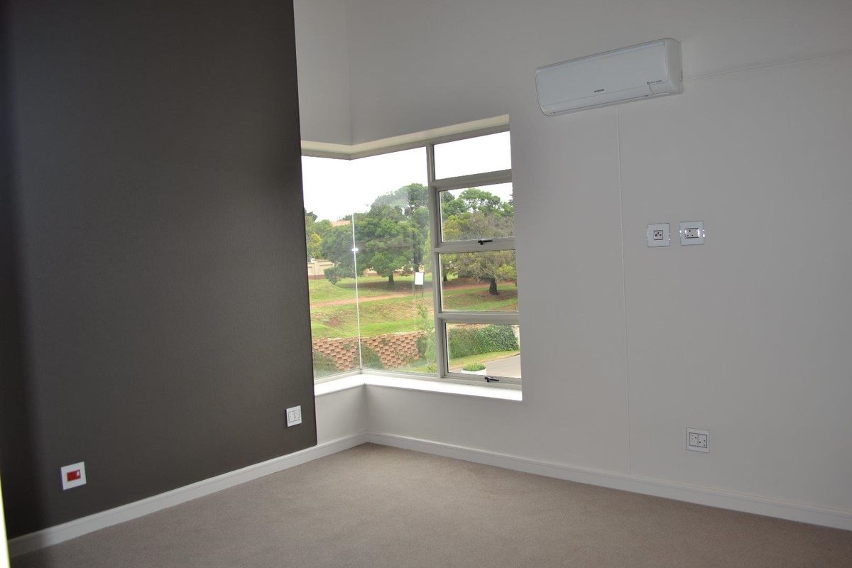 A bright, empty bedroom featuring a corner window, neutral carpeting, and a wall-mounted split-system air conditioner.
