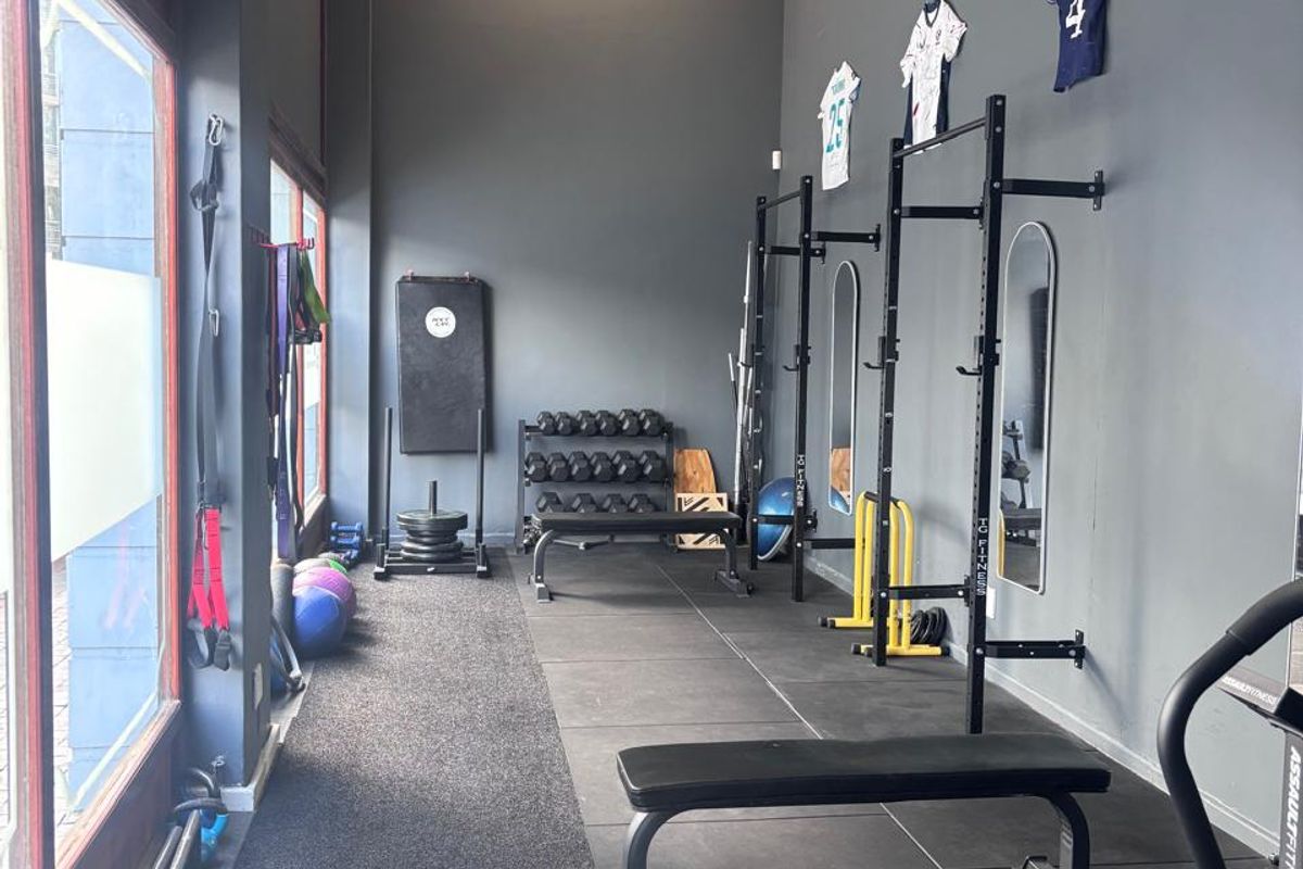 A functional gym space featuring rubberized flooring, wall-mounted squat racks, and large windows providing natural light.