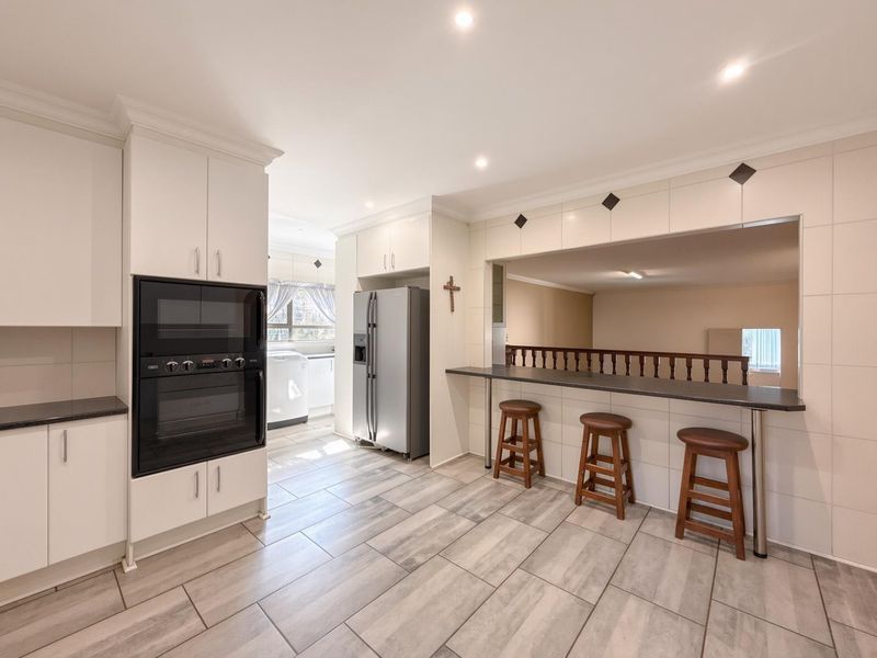A well-maintained kitchen featuring built-in oven and microwave, tiled flooring, and a breakfast bar overlooking an adjacent living space.