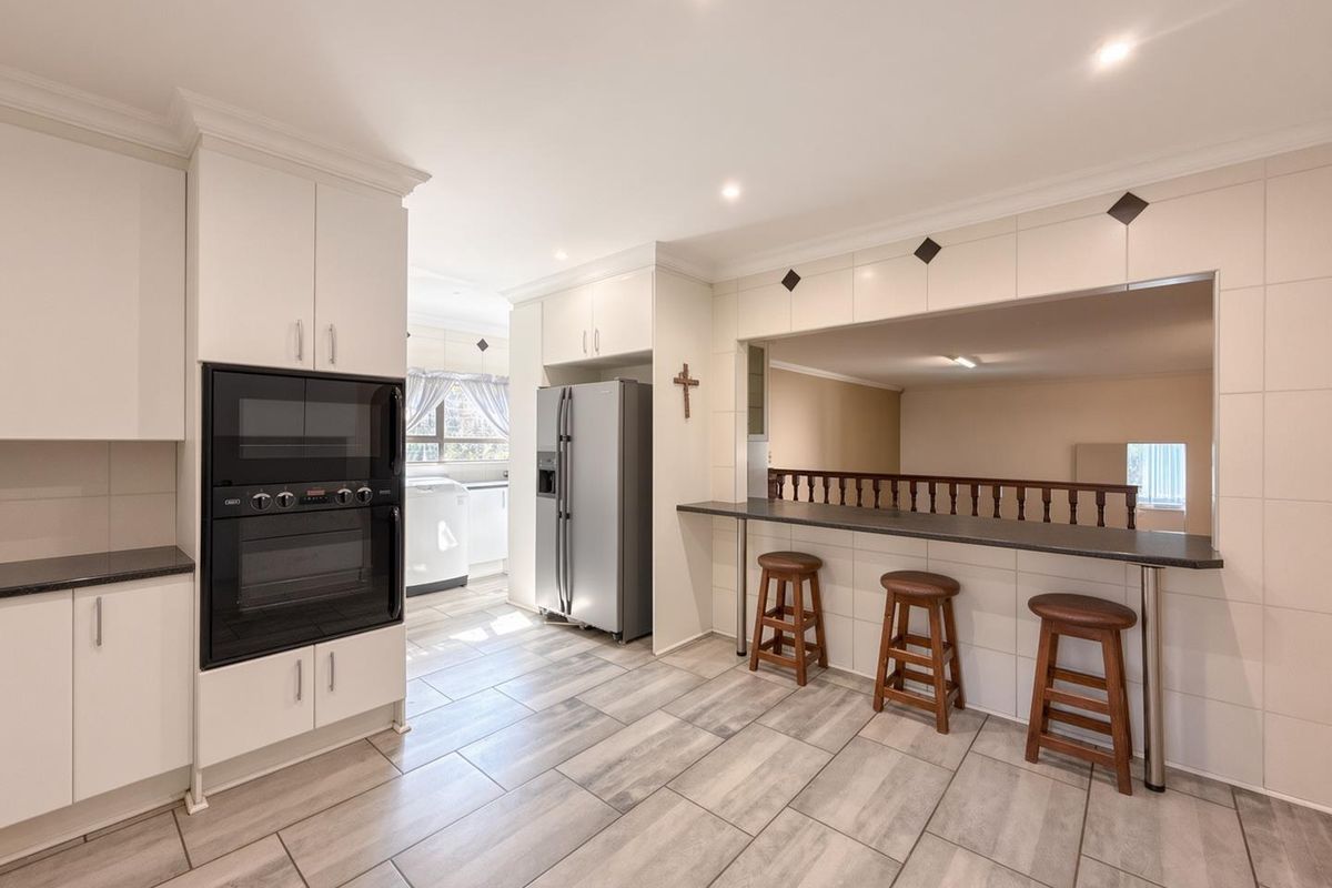 A well-maintained kitchen featuring built-in oven and microwave, tiled flooring, and a breakfast bar overlooking an adjacent living space.