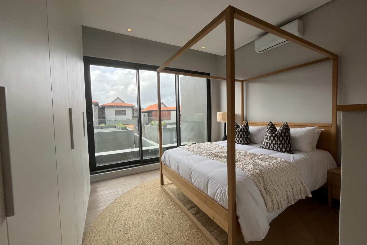 A modern bedroom featuring built-in floor-to-ceiling wardrobes, large sliding glass doors, and a wall-mounted air conditioning unit.