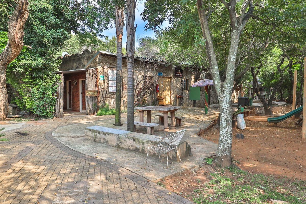 A rustic stone-clad farm building exterior featuring a paved courtyard area with built-in seating, surrounded by mature trees and natural landscaping.