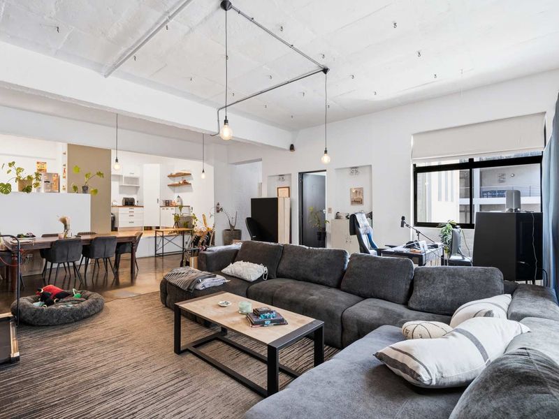 Spacious open-plan office area featuring an industrial-style exposed concrete ceiling, modern lighting, and an integrated kitchen space with ample natural light.