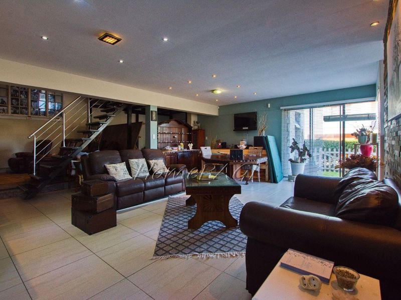 Spacious open-plan living area featuring tiled floors, a stone feature wall, recessed lighting, and a staircase with a modern metal railing.