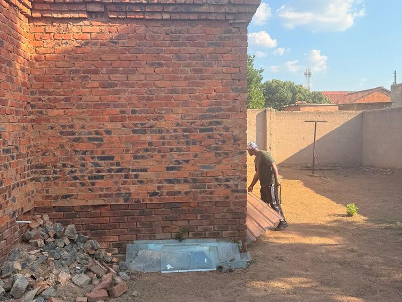 Rear exterior view of the property showing a brick wall structure with surrounding yard space and debris.