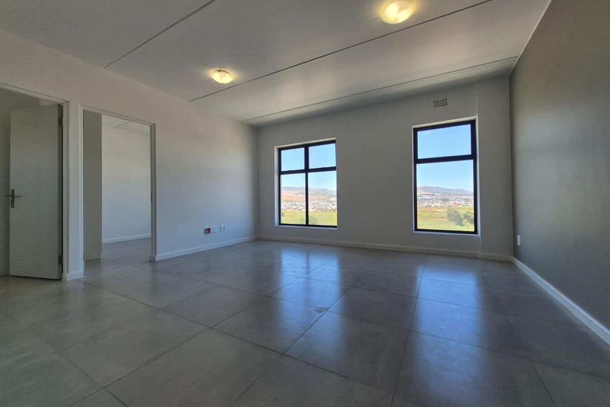 A bright, empty living area featuring large windows with scenic views, tiled flooring, and neutral wall finishes.