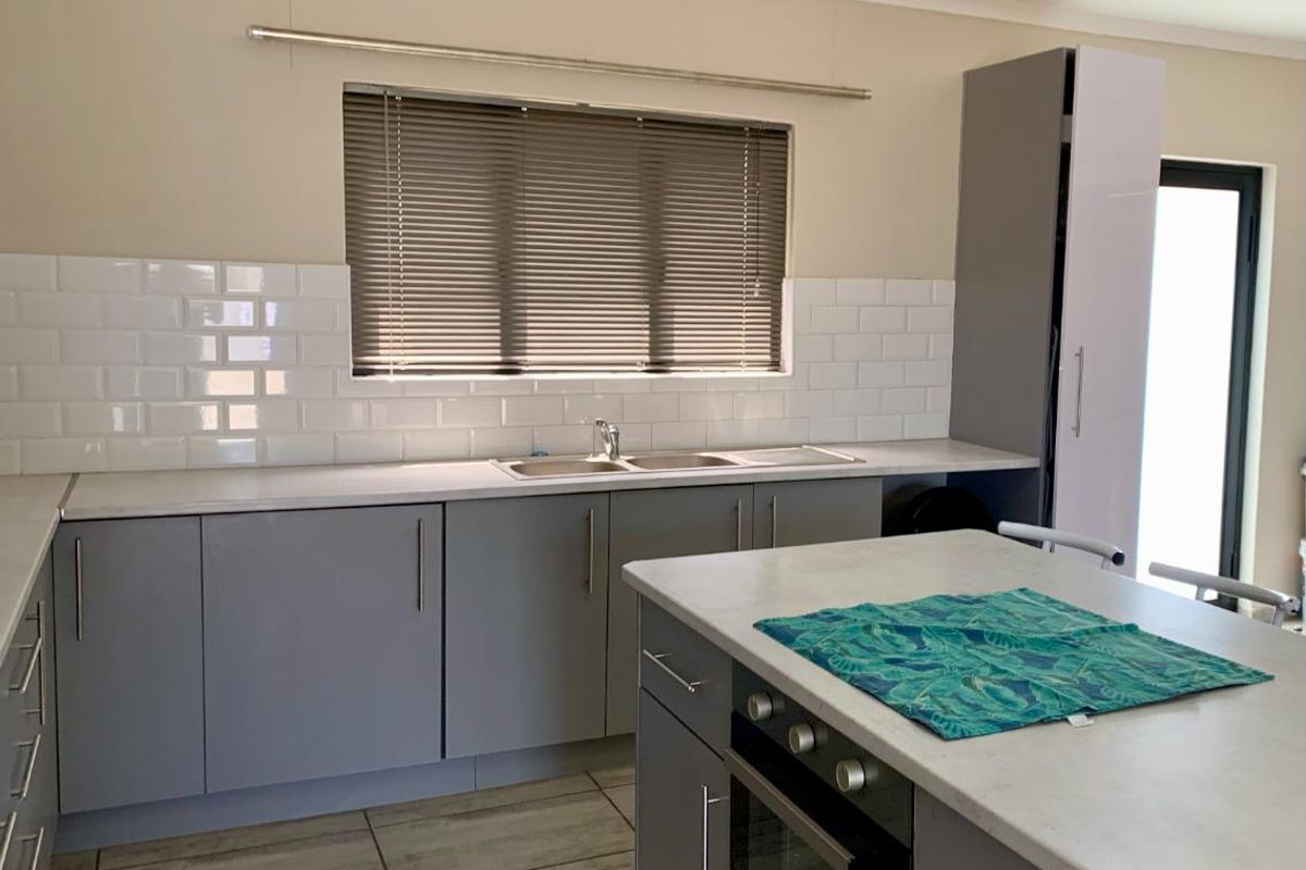 Modern kitchen featuring grey cabinetry, white subway tile backsplash, stone-look countertops, a central island with built-in oven, and tiled flooring.