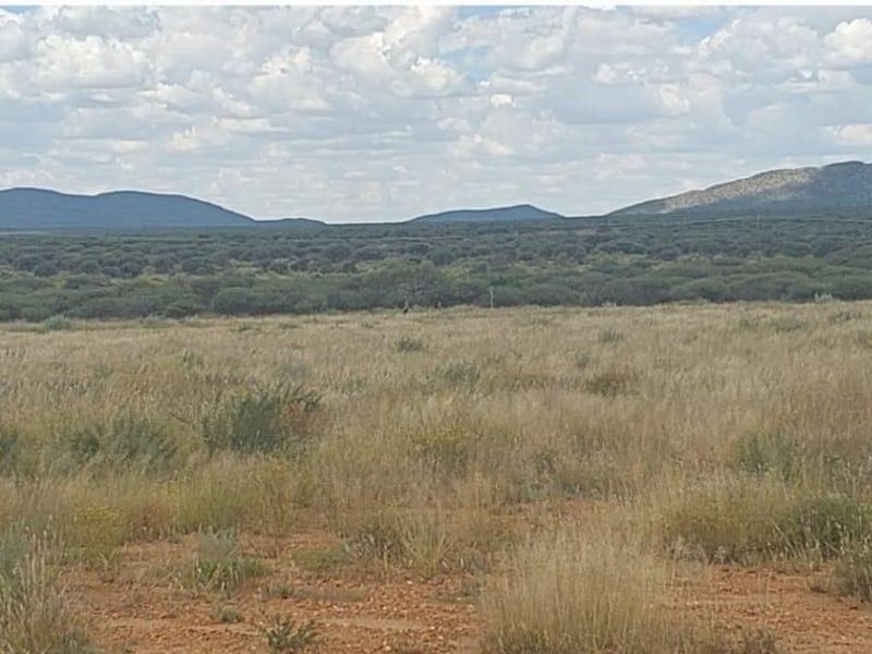 A wide-angle view of the expansive agricultural land featuring natural grassland and distant mountain ranges under a cloudy sky.