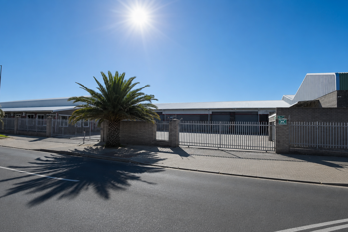 Front exterior view of an industrial property featuring secure perimeter fencing, brick boundary walls, and multiple roller shutter access doors.