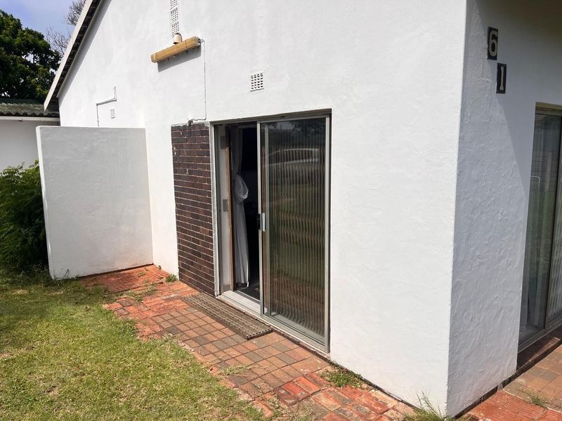 Rear exterior view of the property featuring a sliding glass door, brick paving, and white rendered walls.