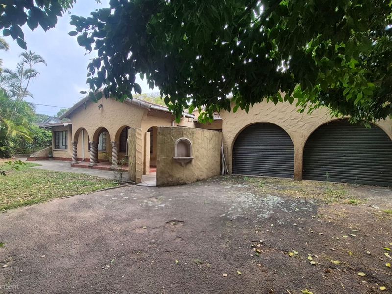 Front elevation of a house featuring a double garage, arched portico with decorative columns, and a textured stucco facade with an asphalt driveway.