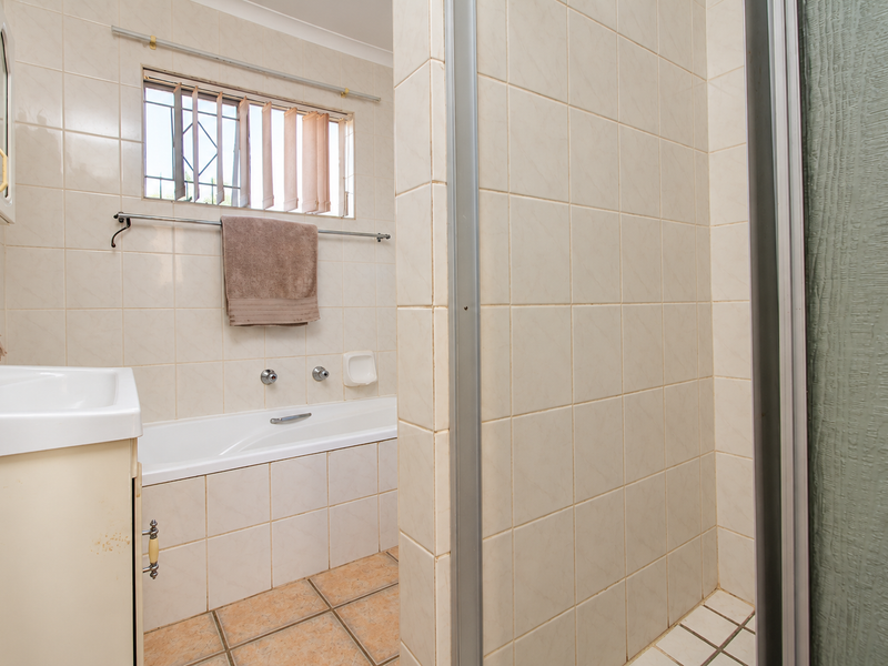 A functional bathroom featuring a built-in bathtub, separate shower enclosure, and a vanity basin with tiled finishes throughout.