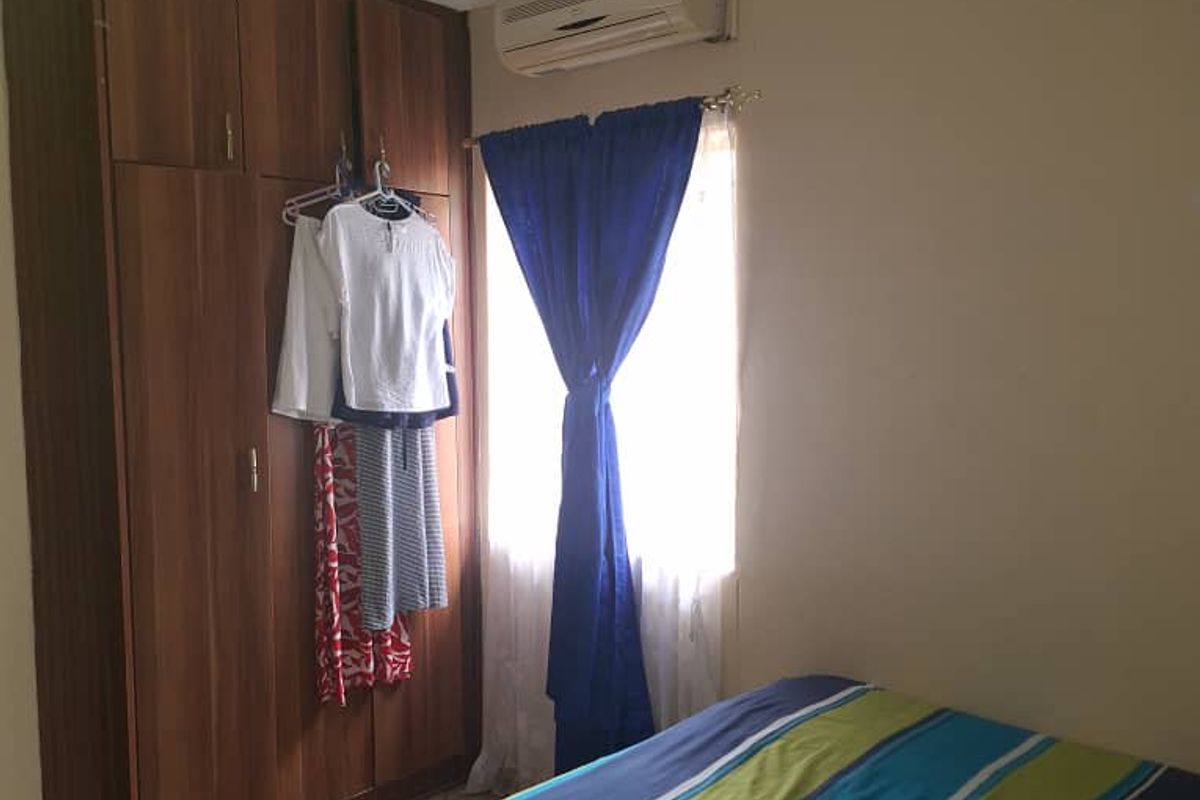 A bedroom featuring built-in wooden cupboards, tiled flooring, and a wall-mounted air conditioning unit.