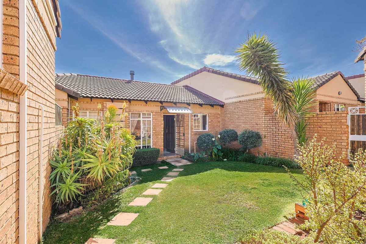 A well-maintained rear garden featuring a brick facade, tiled roof, and a neat lawn with paved stepping stones leading to the entrance.