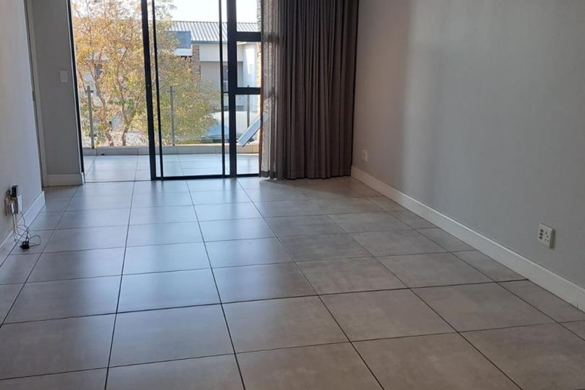 A bright, empty living room featuring large format floor tiles, neutral walls, and a sliding glass door leading to an outdoor balcony area.