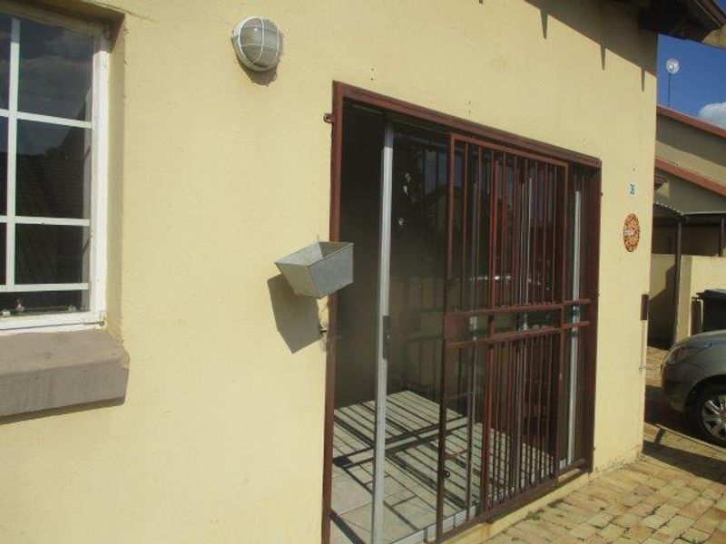 Exterior view of the apartment entrance featuring a sliding glass door with a security gate and a paved driveway area.