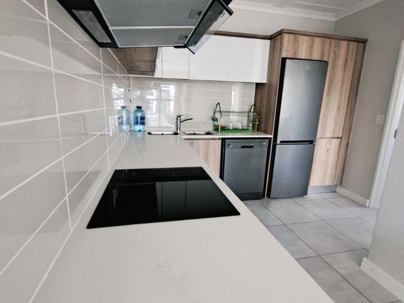 Modern kitchen featuring sleek white and wood-grain cabinetry, stone countertops, integrated electric hob, extractor fan, and tiled finishes throughout.