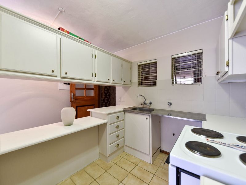 A functional kitchen featuring built-in cabinetry, a stainless steel sink, tiled splashback, and ceramic tile flooring, offering a practical layout for daily use.
