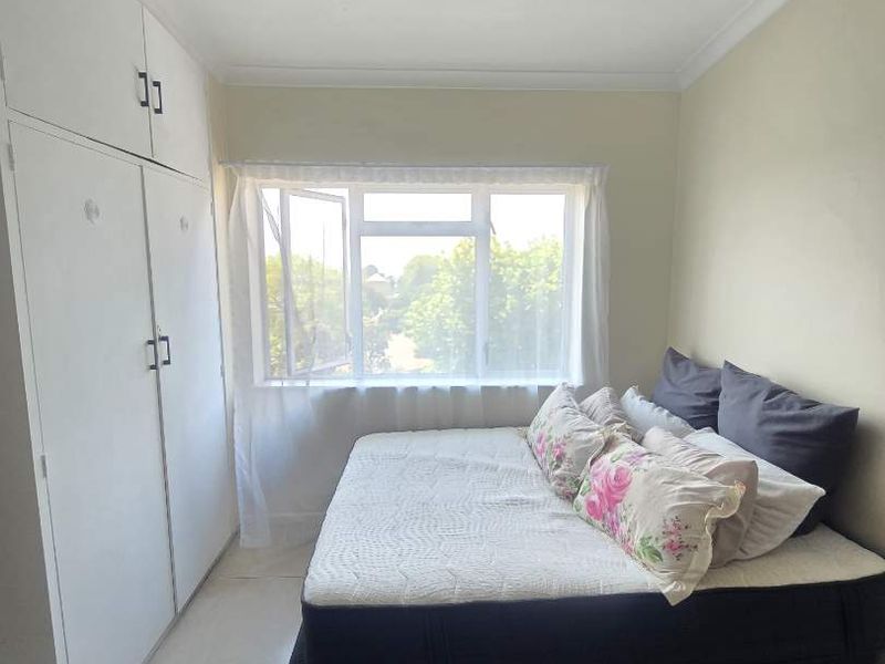 A functional bedroom featuring built-in cupboards, neutral tiled flooring, and a large window providing natural light.
