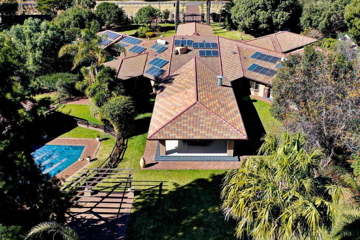 Aerial view of a residential property featuring a large tiled roof with integrated solar panels, a swimming pool, and established garden areas.