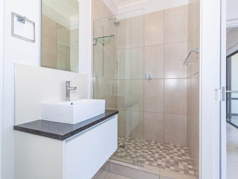 Modern bathroom featuring a floating vanity with a vessel sink, a glass-enclosed shower with mosaic floor tiles, and neutral wall tiling.