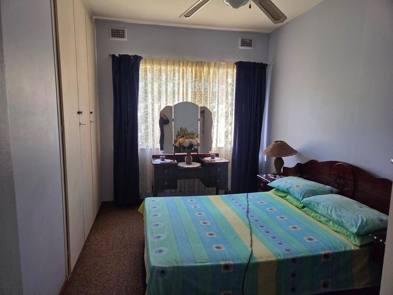 A bedroom featuring built-in cupboards, carpet flooring, and a ceiling fan, offering a functional space with potential for modern updates.