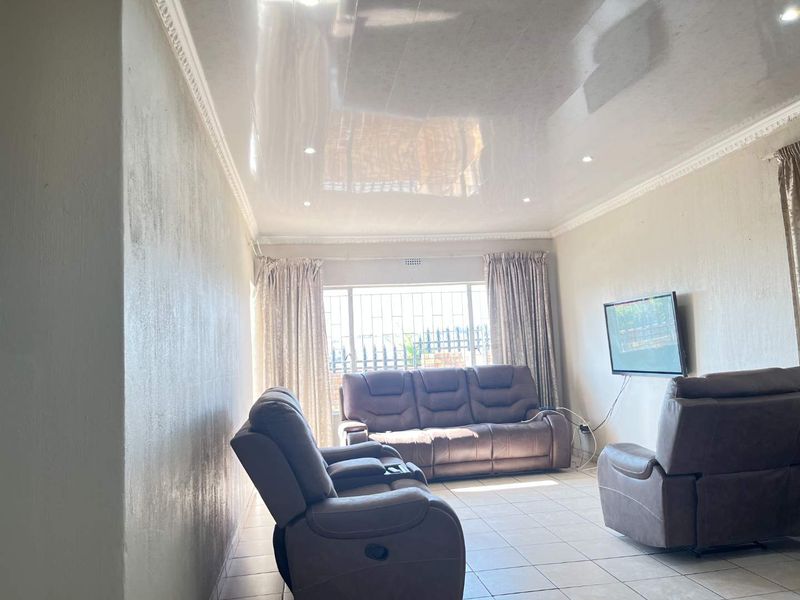 A living room featuring a glossy stretch ceiling, recessed lighting, ceramic floor tiles, and security burglar bars on the window.