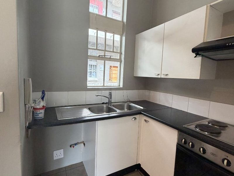 Compact kitchen featuring built-in cabinetry, electric oven with hob, stainless steel sink, and tiled flooring. Requires minor repairs to cabinetry and plumbing.