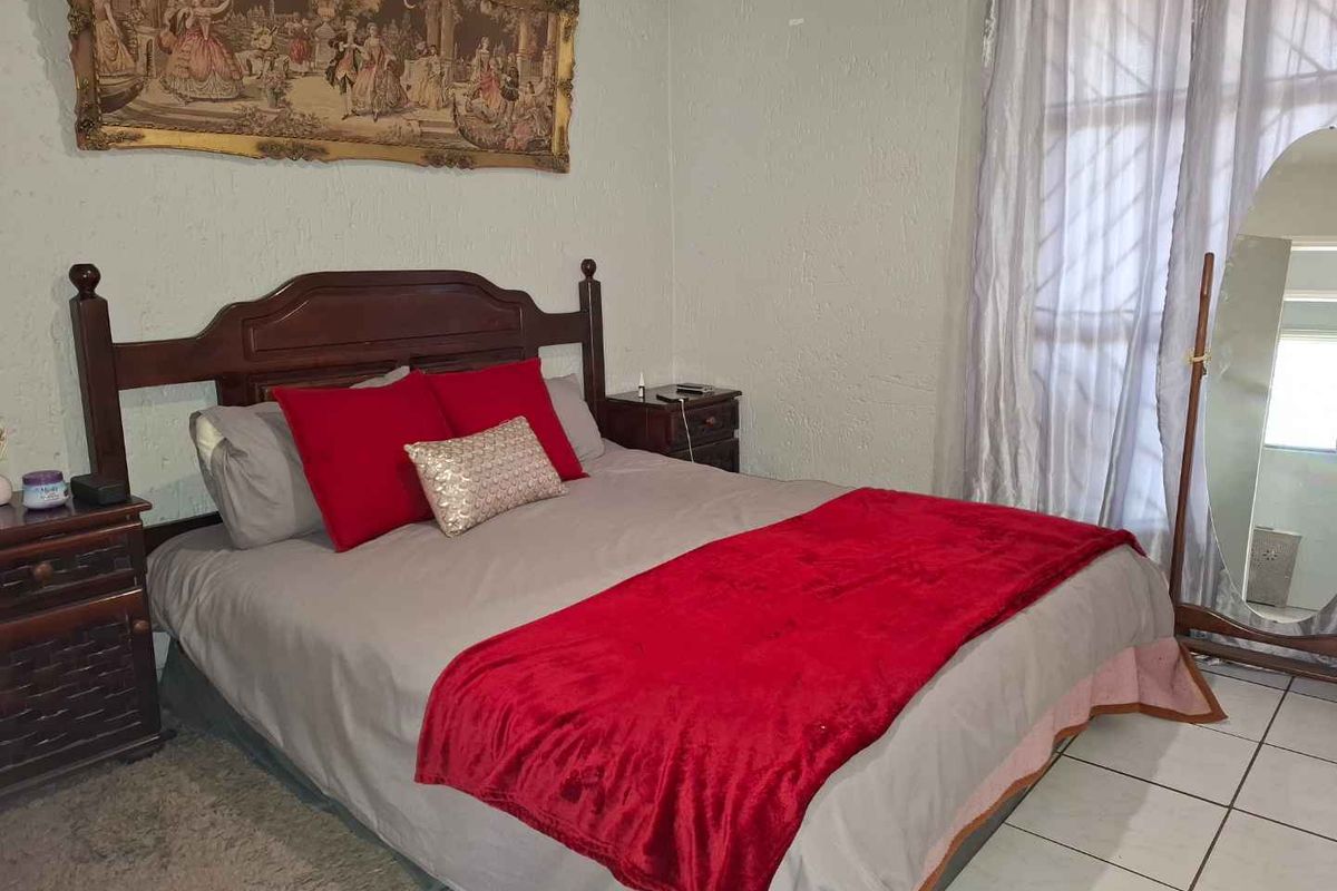 A bedroom featuring tiled flooring and a window with security bars, providing a functional space for rest.