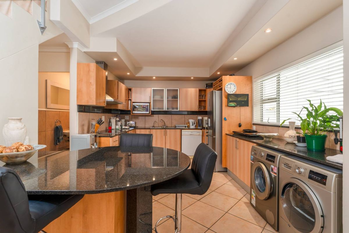 Functional kitchen featuring granite countertops, laminate cabinetry, integrated appliances, and tiled flooring, offering a practical layout with an attached breakfast bar.