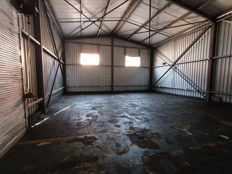 Spacious industrial utility space featuring exposed steel roof trusses, corrugated metal walls, and a large roller shutter door with worn concrete flooring.