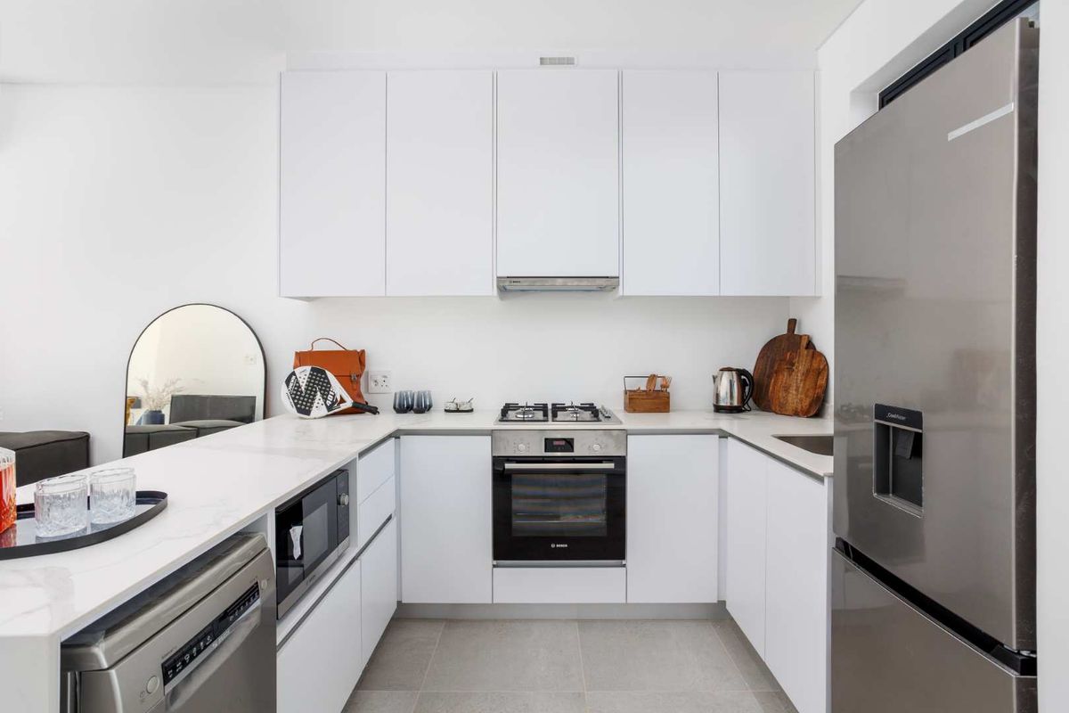 Modern kitchen featuring sleek white cabinetry, stone countertops, high-quality built-in appliances, and a functional U-shaped layout with tiled flooring.